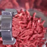 Mielone mięso wychodzi z metalowej kruszarki do kruszywa, tworząc stosik na tle naczynia.