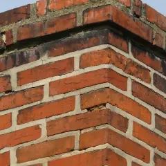 Ceglany komin, widać ile cegieł na komin, z niebieskim niebem w tle.