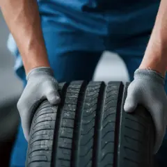 Mechanik w szarych rękawiczkach trzyma oponę radialną.