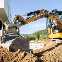 Żółta koparka z zamontowaną kruszarką do koparki pracuje na budowie, przygotowując teren pod nowy dom.