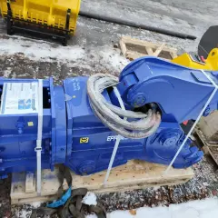 Solidne nożyce hydrauliczne do koparki, gotowe do pracy. W tle żółte i pomarańczowe łyżki.