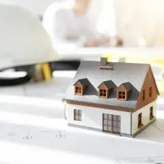 Model domu na planach, kask budowlany i poziomica. Zastanawiasz się, ile kosztuje budowa garażu?