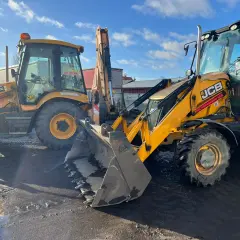 Dwie żółte koparki JCB stoją na błotnistym placu. Czy na koparkę trzeba mieć prawo jazdy? Sprawdź na stronie www.inzynieria.org.