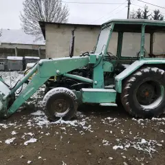 Zielona koparka Ostrówek stoi na błotnistym terenie, pokryta śniegiem.