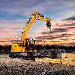 Operator koparki kurs: żółta maszyna JCB podnosi ciężki element na tle zachodzącego słońca.