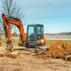 Pomarańczowa minikoparka na placu budowy. Zastanawiasz się, ile kosztuje godzina pracy minikoparki? Ta maszyna jest gotowa do pracy.