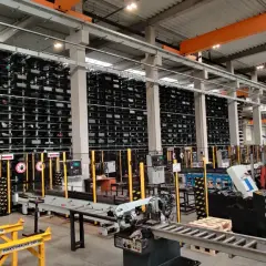 Magazyn z regałami pełnymi materiałów, w tym różnych gatunków stali trudnościeralnej. Pracownik w kamizelce odblaskowej przy maszynie.