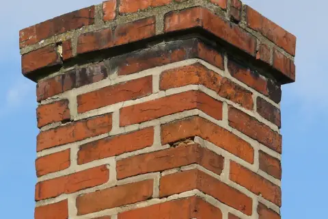 Ceglany komin, widać ile cegieł na komin, z niebieskim niebem w tle.