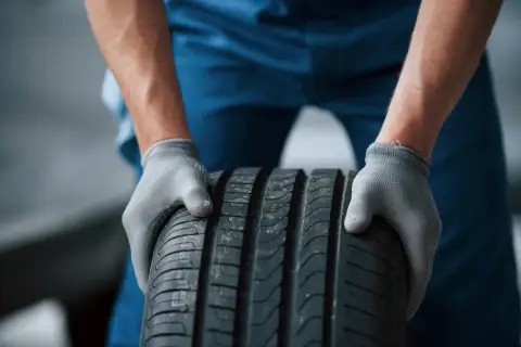 Mechanik w szarych rękawiczkach trzyma oponę radialną.