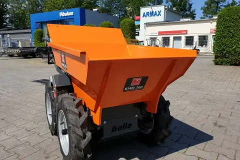 Pomarańczowe, małe wozidła budowlane stoją na placu przed budynkami.