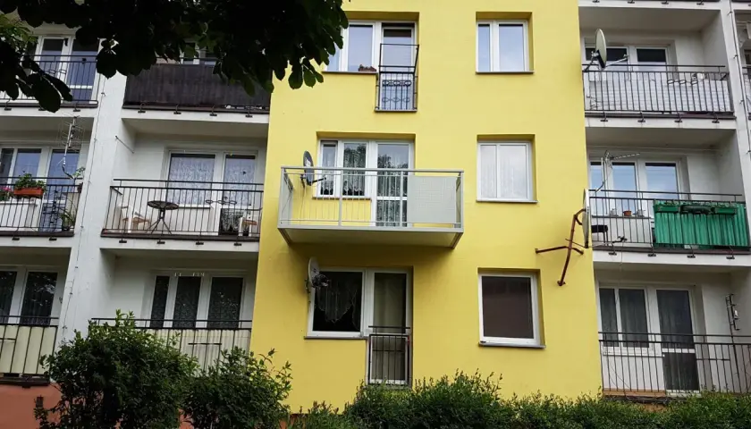 Żółty blok z balkonami. Widać, jak przedłużyć balkon betonowy, dodając nowoczesną, metalową konstrukcję.