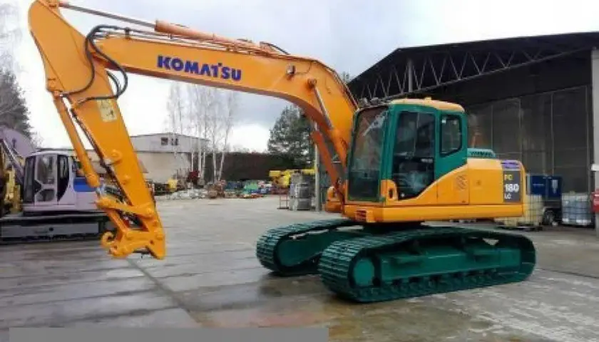 Pomarańczowa koparka gąsienicowa Komatsu PC 180 LC z zielonym podwoziem stoi na placu budowy.
