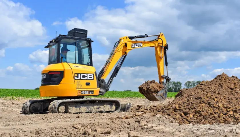 Żółte mini koparki JCB pracują na budowie, kopiąc ziemię.