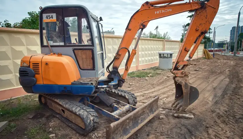 Pomarańczowa koparka Hitachi z gąsienicami i szerokim lemieszem do koparki, gotowa do pracy na budowie.