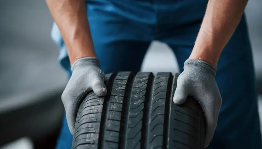 Mechanik w szarych rękawiczkach trzyma oponę radialną.