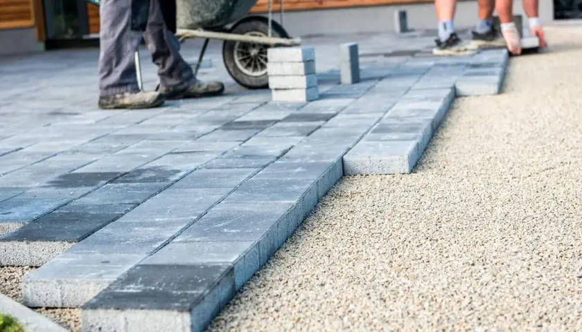 Układanie płyt betonowych na żwirze – tania alternatywa dla kostki brukowej. Pracownicy budują taras.