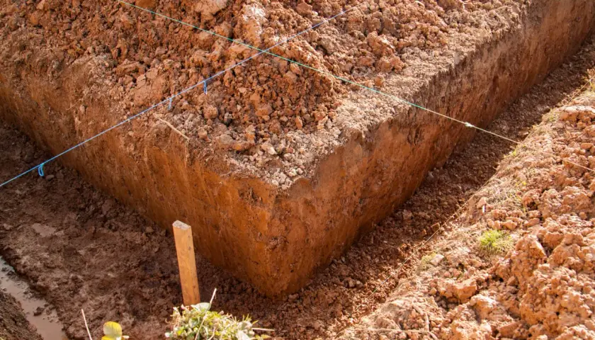 Wykonano wykop pod ławy fundamentowe. Widać ziemię, sznurki wyznaczające linie i drewniany palik.