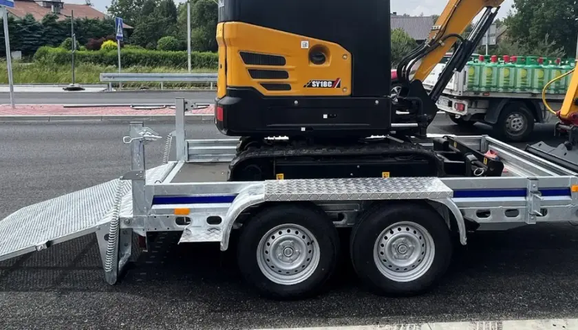 Żółta minikoparka SY18C na przyczepie. Zastanawiasz się, ile waży minikoparka? Ta jest gotowa do transportu.
