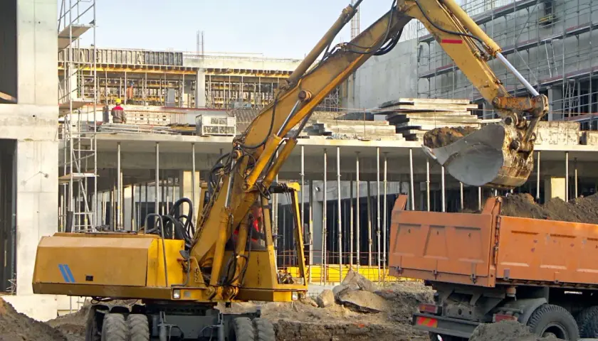 Koparka z uprawnieniami na maszyny budowlane zasypuje ziemią wywrotkę na placu budowy.