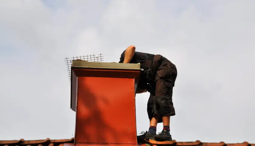 Pracownik na dachu sprawdza komin. Dowiedz się, ile kosztuje naprawa komina na dachu, gdy wymaga prac wysokościowych.