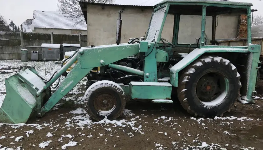 Zielona koparka Ostrówek stoi na błotnistym terenie, pokryta śniegiem.