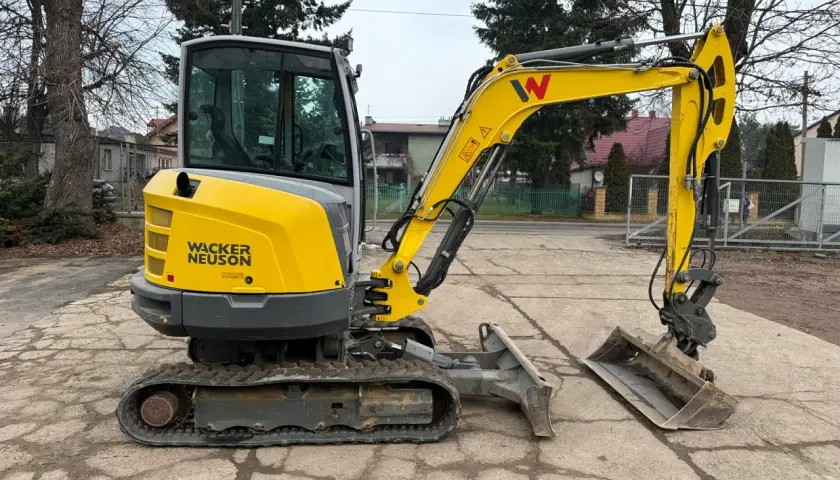 Żółta minikoparka Wacker Neuson z kabiną stoi na placu.