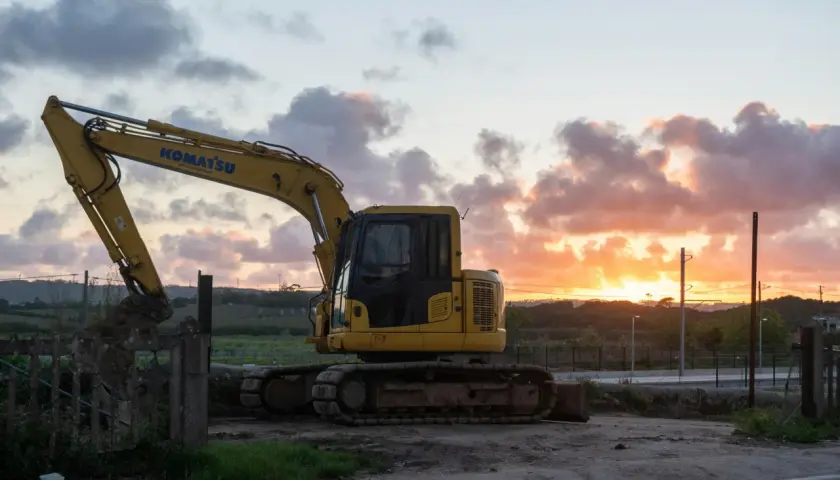 Żółta koparka Komatsu na tle zachodzącego słońca. Maszyna gotowa do pracy, nawet gdy dzień dobiega końca.