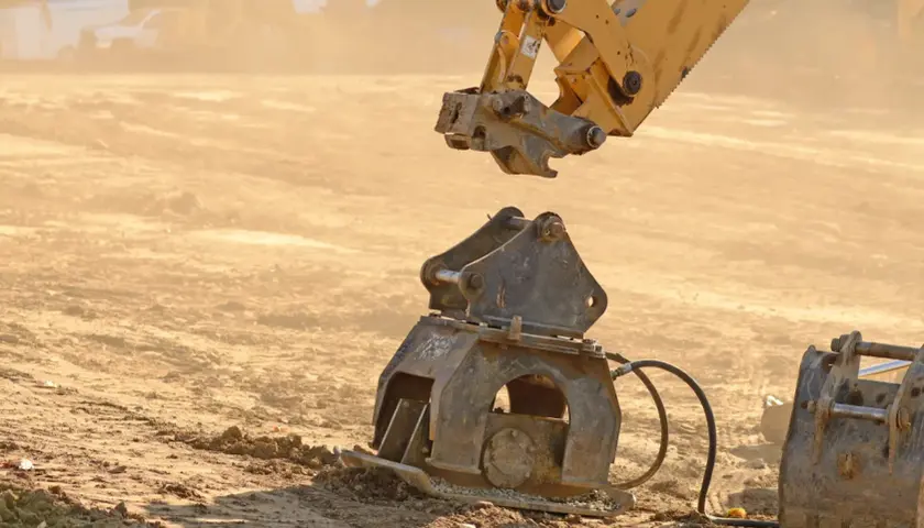 Żółty osprzęt koparki przygotowuje się do połączenia z ubijakiem. Widoczny mechanizm mocowania łyżki koparki.