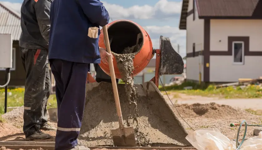 Robotnicy mieszają beton w betoniarce. Z jednego worka cementu powstaje spora ilość materiału budowlanego.