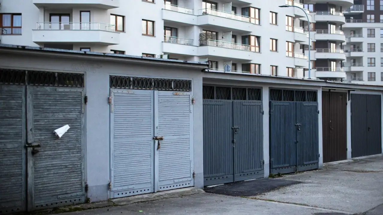 Rząd garaży wolnostojących zamykanych na kłódki, na tle nowoczesnego bloku mieszkalnego. Zastanawiasz się, ile kosztuje garaż wolnostojący?