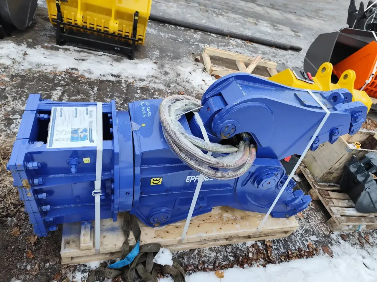 Solidne nożyce hydrauliczne do koparki, gotowe do pracy. W tle żółte i pomarańczowe łyżki.