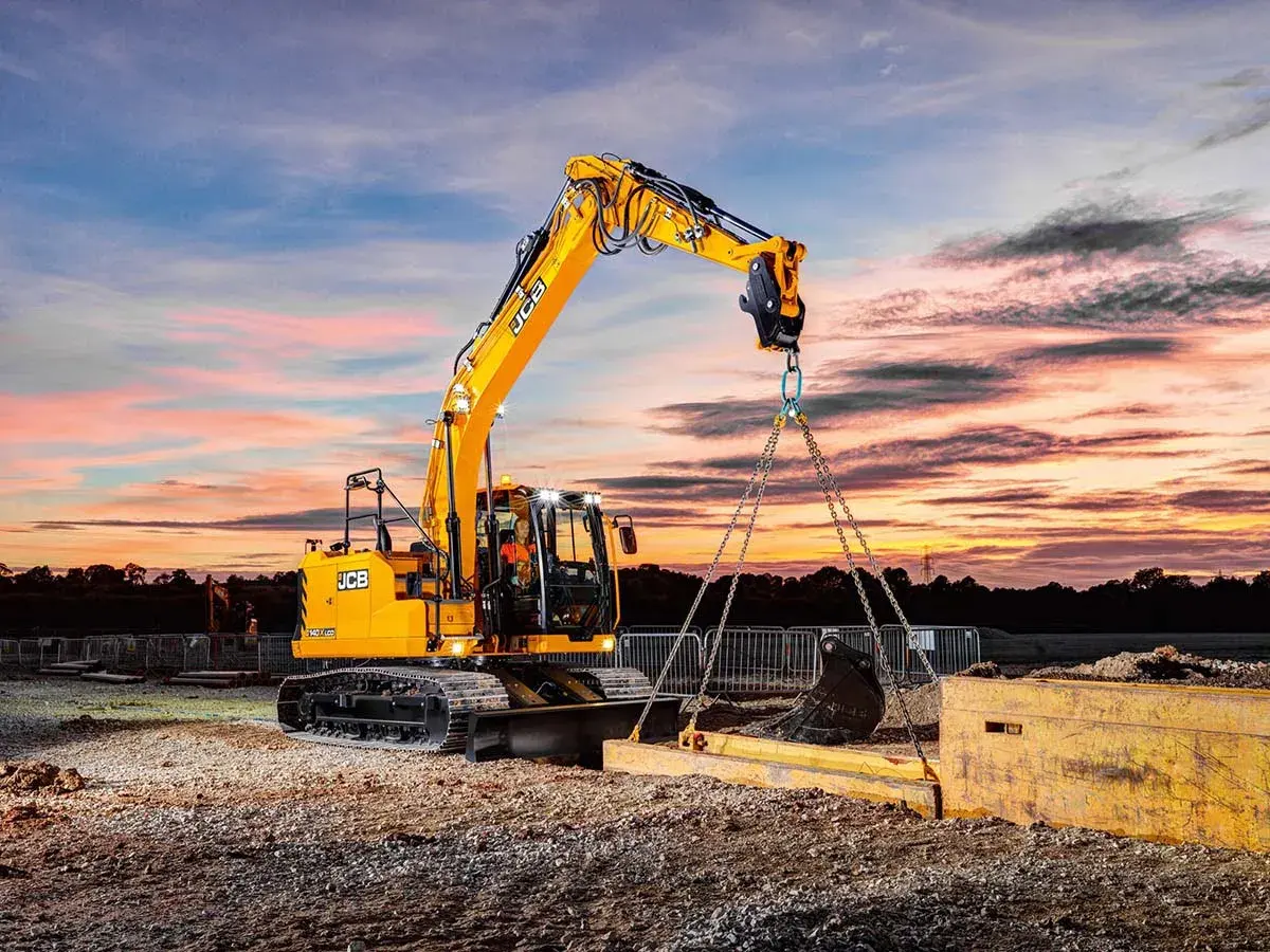 Operator koparki kurs: żółta maszyna JCB podnosi ciężki element na tle zachodzącego słońca.