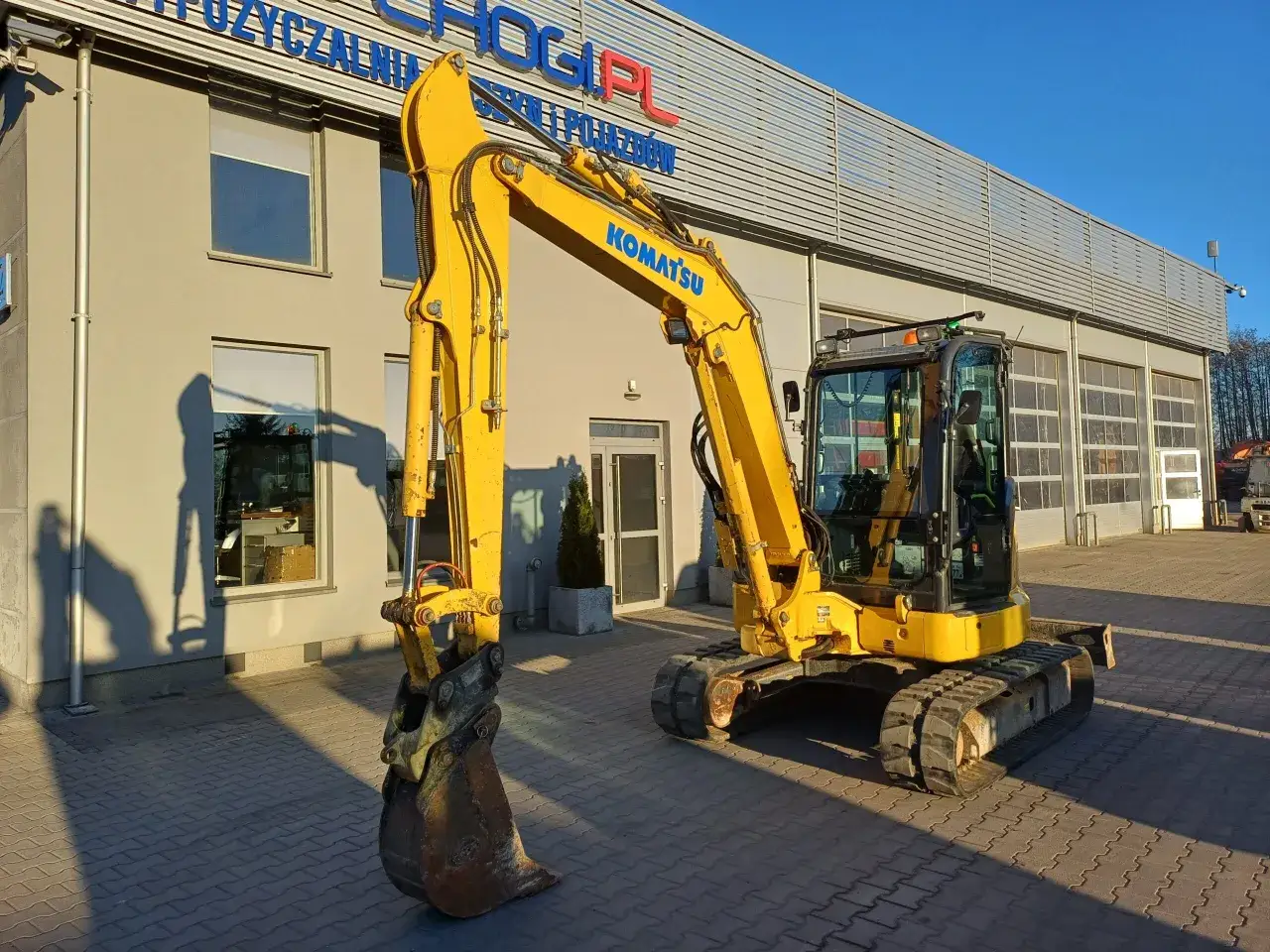 Żółta koparka Komatsu przed budynkiem z napisem 