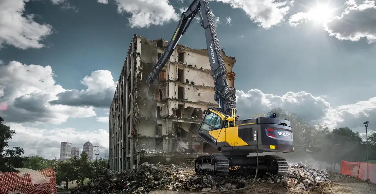 Potężna koparka do rozbiórek Volvo EC480E pracuje przy burzeniu wysokiego budynku, rozsypując gruz.