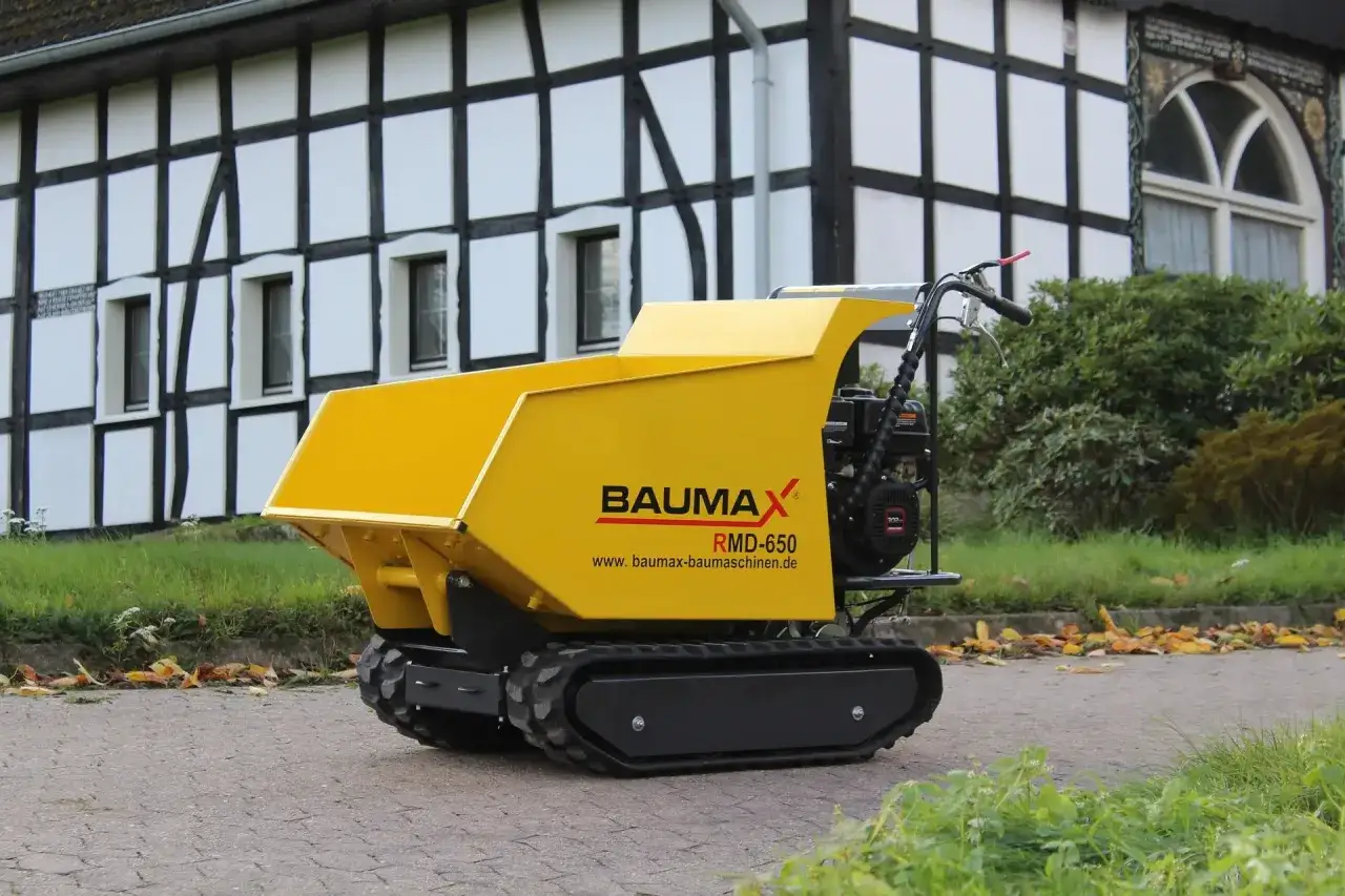 Żółte, gąsienicowe małe wozidła budowlane Baumax RMD-650 gotowe do pracy przy tradycyjnym domu.