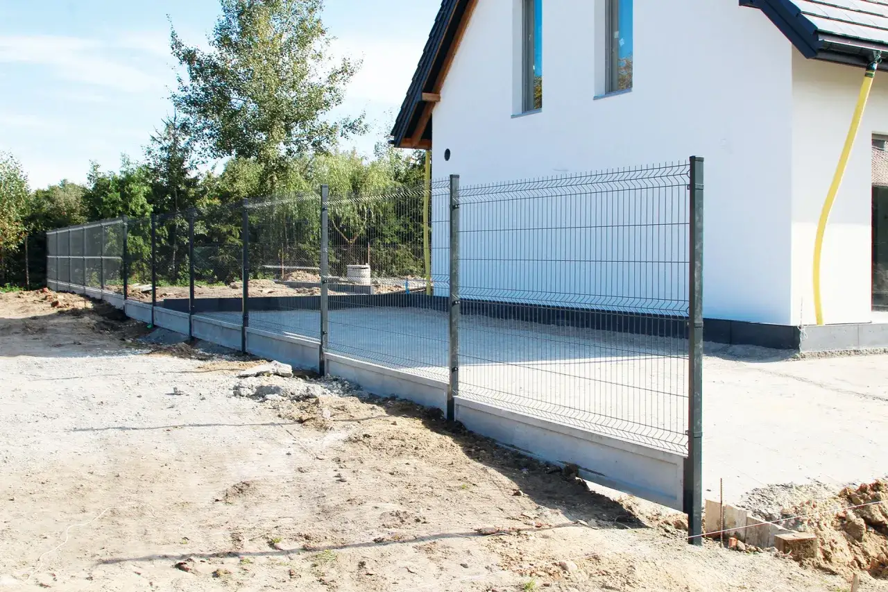 Nowy płot z betonowym podmurówką przy domu. Zastanawiasz się, ile kosztuje wylanie fundamentu pod ogrodzenie?