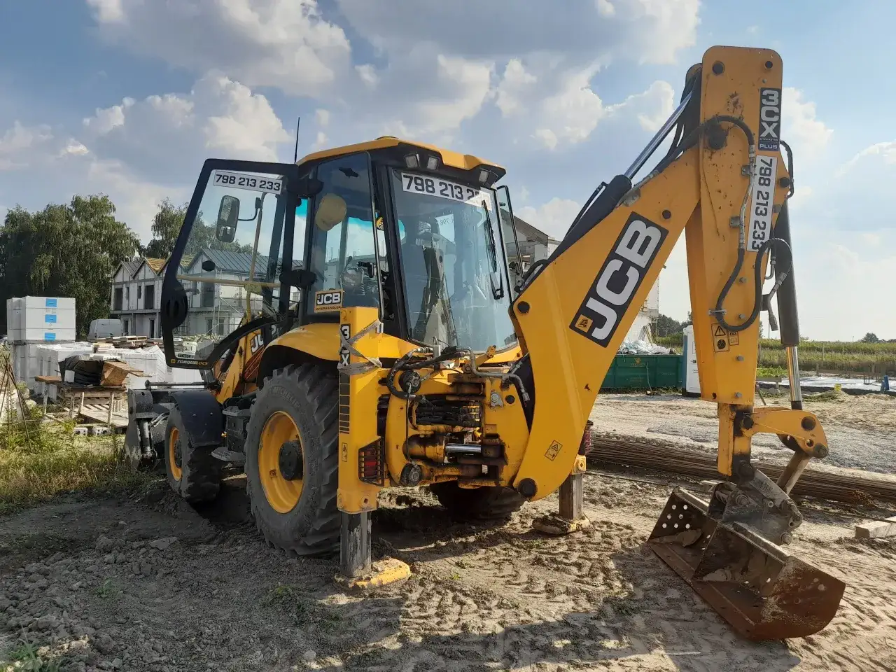 Żółta koparko-ładowarka JCB na placu budowy, gotowa do przyjęcia zleceń na koparko ładowarkę. Numer telefonu 798 213 233.
