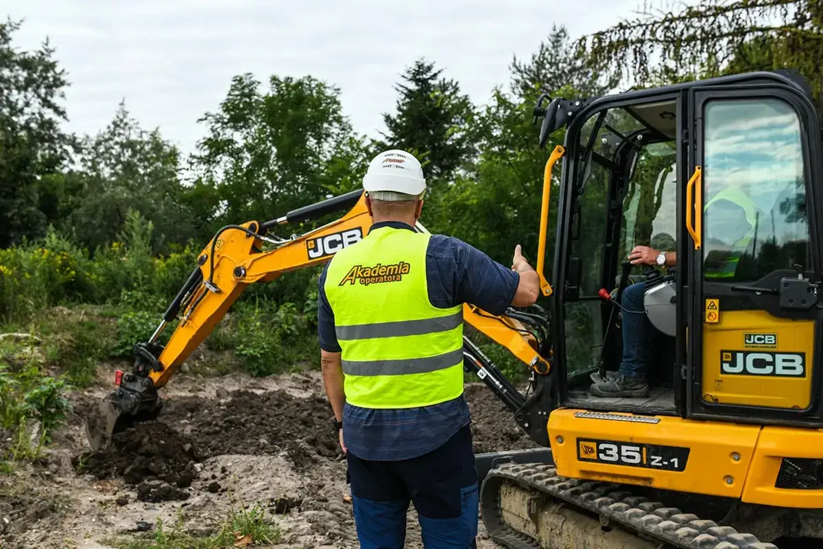 Szkolenie na koparkę, zdobywanie uprawnień na koparkę UDT. Instruktor pokazuje obsługę maszyny.