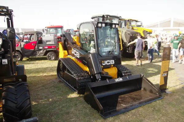 Głównym elementem jest minikoparka gąsienicowa JCB. W tle widać inne maszyny rolnicze i ludzi. Możliwe, że to wystawa, gdzie można sprawdzić jcb polska cennik.